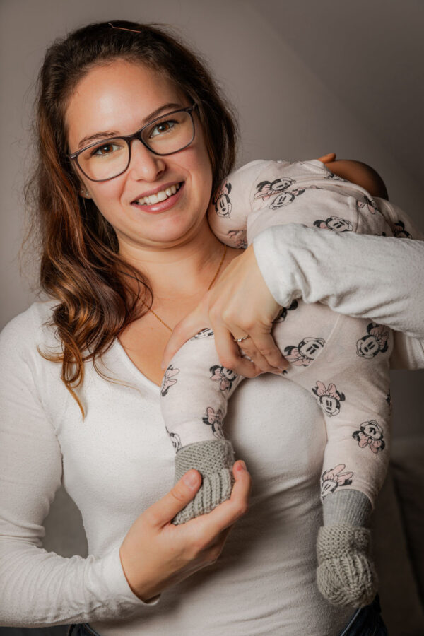 Trageberaterin von SchaukelHerz hält eine Tragepuppe im Diagonalstützgriff und schaut direkt in die Kamera – sichere Tragetechnik demonstriert.