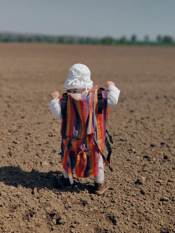 Blog Kleinkind trägt stolz eine Tragehilfe auf dem Rücken und läuft ins weite Feld.